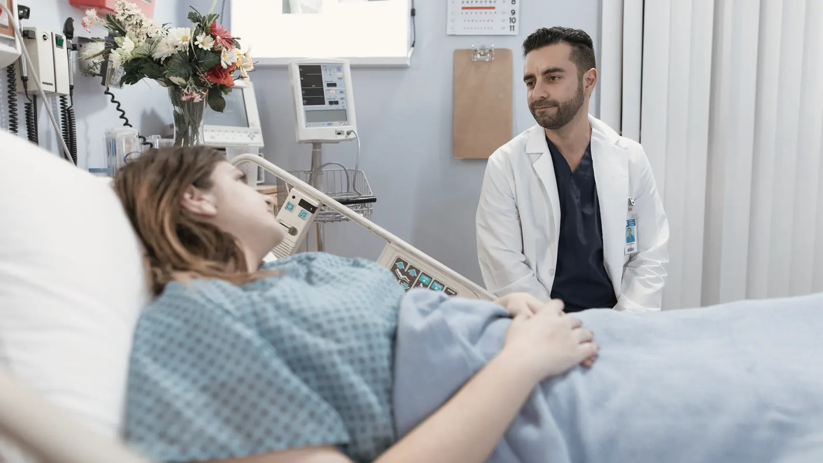 Un médico platica con su paciente, que descansa en una cama de hospital.